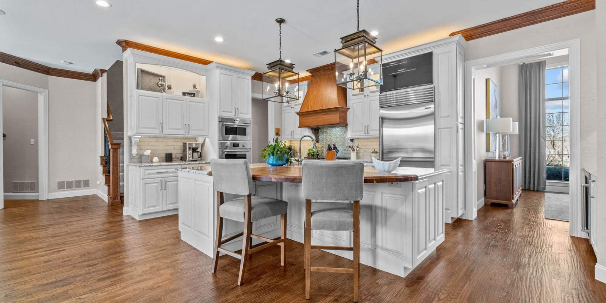 Traditional kitchen design with white cabinets and a wood range hood centerpiece in Frisco, TX