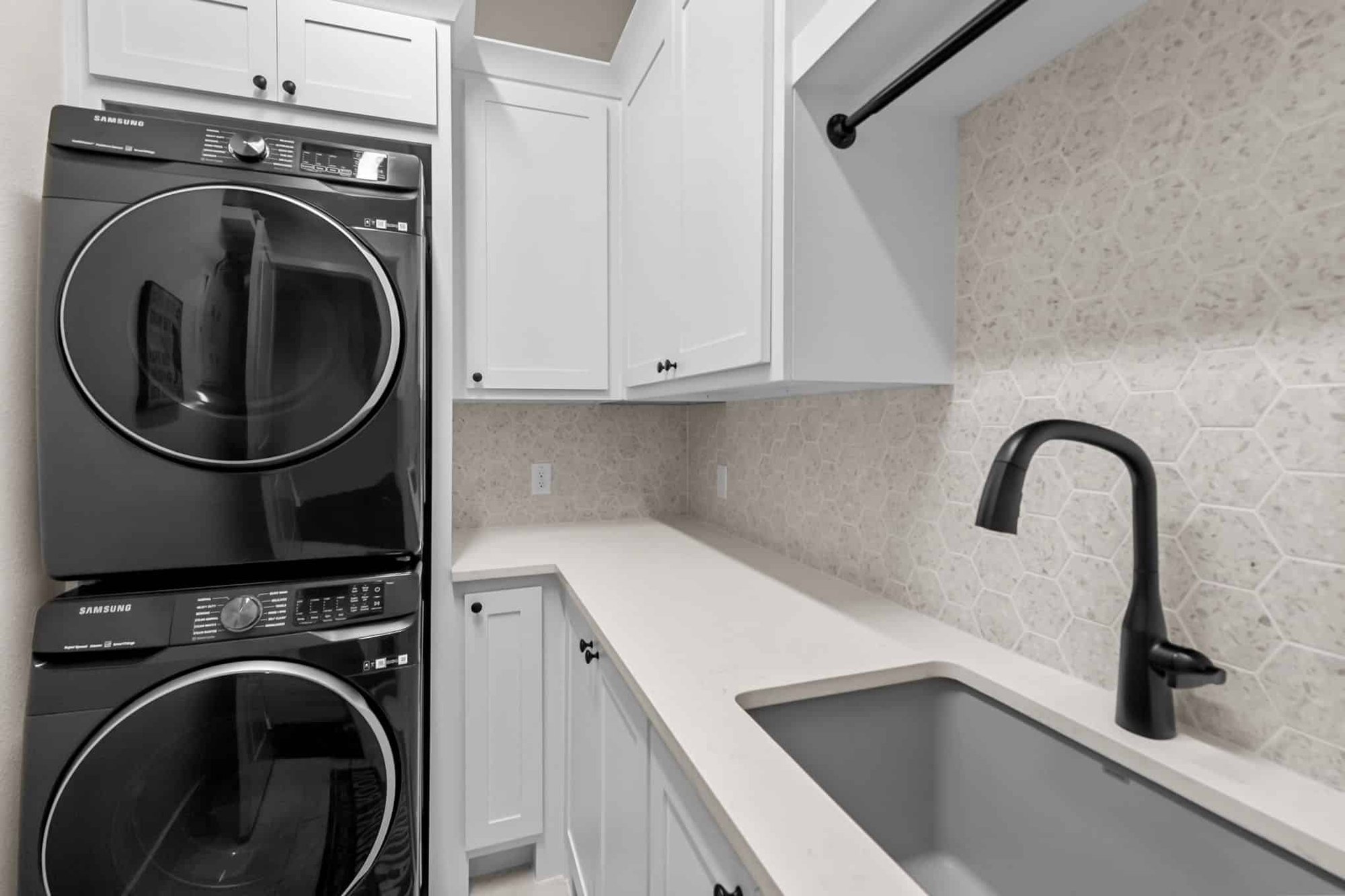 Custom remodeled laundry room in Frisco, TX featuring white cabinetry, black stacked front-load washer and dryer