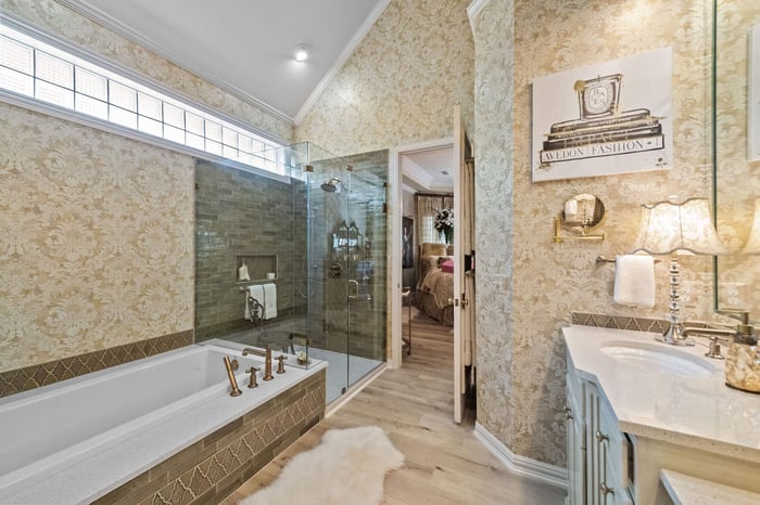 Custom remodeled primary bathroom in Frisco, TX featuring gold patterned wallpaper and glass enclosed shower