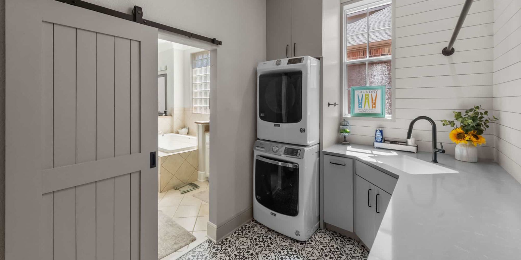 Image of a remodeled laundry room with stacked washer and dryer, sink, and rustic sliding door in Frisco, TX